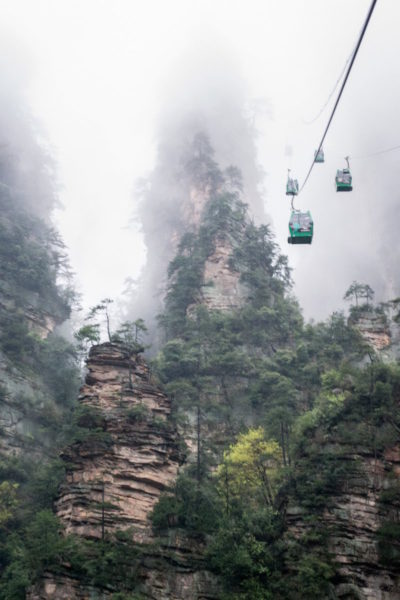 The cable car at Zhangjiajie disappears into fog between jagged mountains.